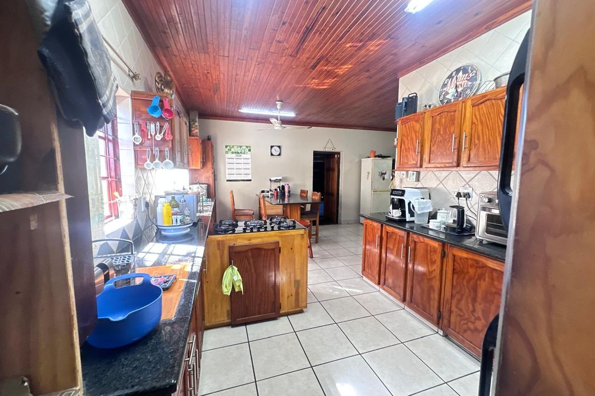 A functional kitchen featuring wooden cabinetry, granite countertops, a gas hob, and a distinctive wooden tongue and groove ceiling with tiled flooring.