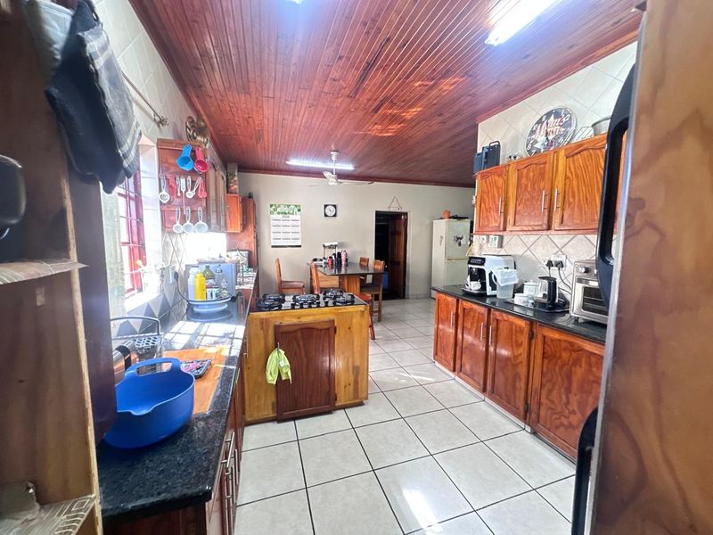 A functional kitchen featuring wooden cabinetry, granite countertops, a gas hob, and a distinctive wooden tongue and groove ceiling with tiled flooring.