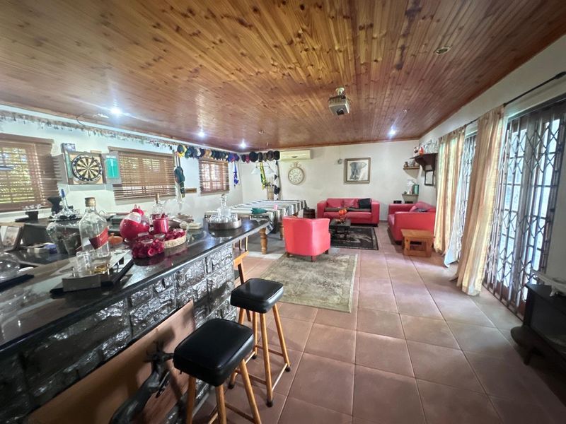 Spacious open-plan living area featuring a built-in bar, tiled flooring, and a timber-clad ceiling with direct access to the outdoors via sliding doors.