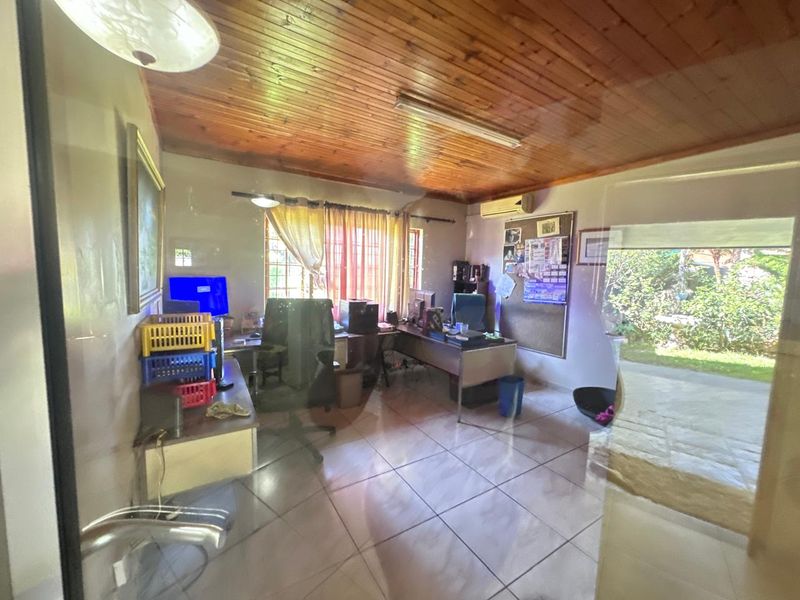 A functional home office space featuring a timber ceiling, tiled flooring, and direct access to the garden through a sliding glass door.