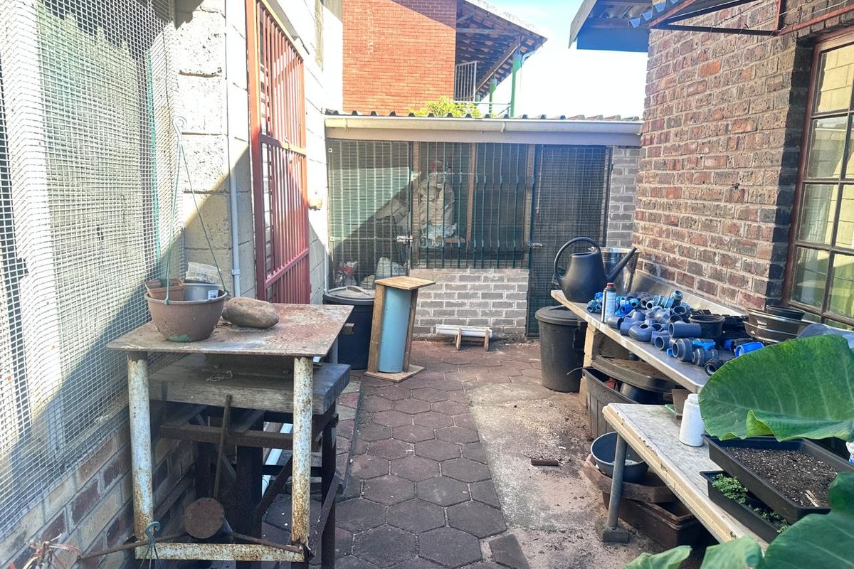A utilitarian rear exterior area featuring brick paving, exposed brick walls, and secure metal mesh enclosures, suitable for storage or workshop use.