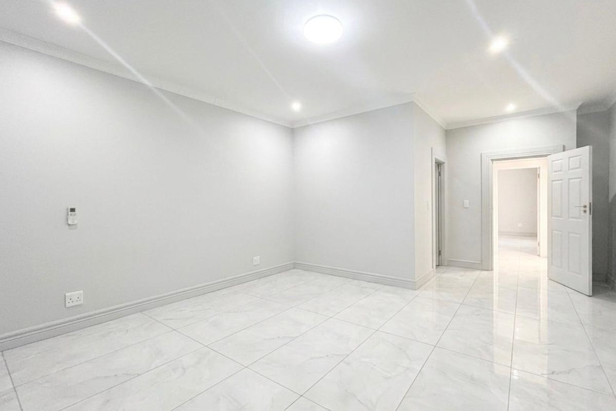 A bright, empty living area featuring modern white marble-look floor tiles, recessed downlighting, and clean neutral wall finishes.