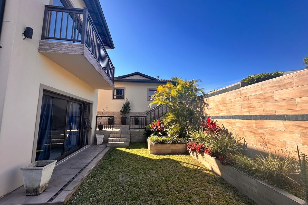 A well-maintained rear garden featuring a tiled patio, raised planter beds, and a balcony overlooking the landscaped outdoor space.