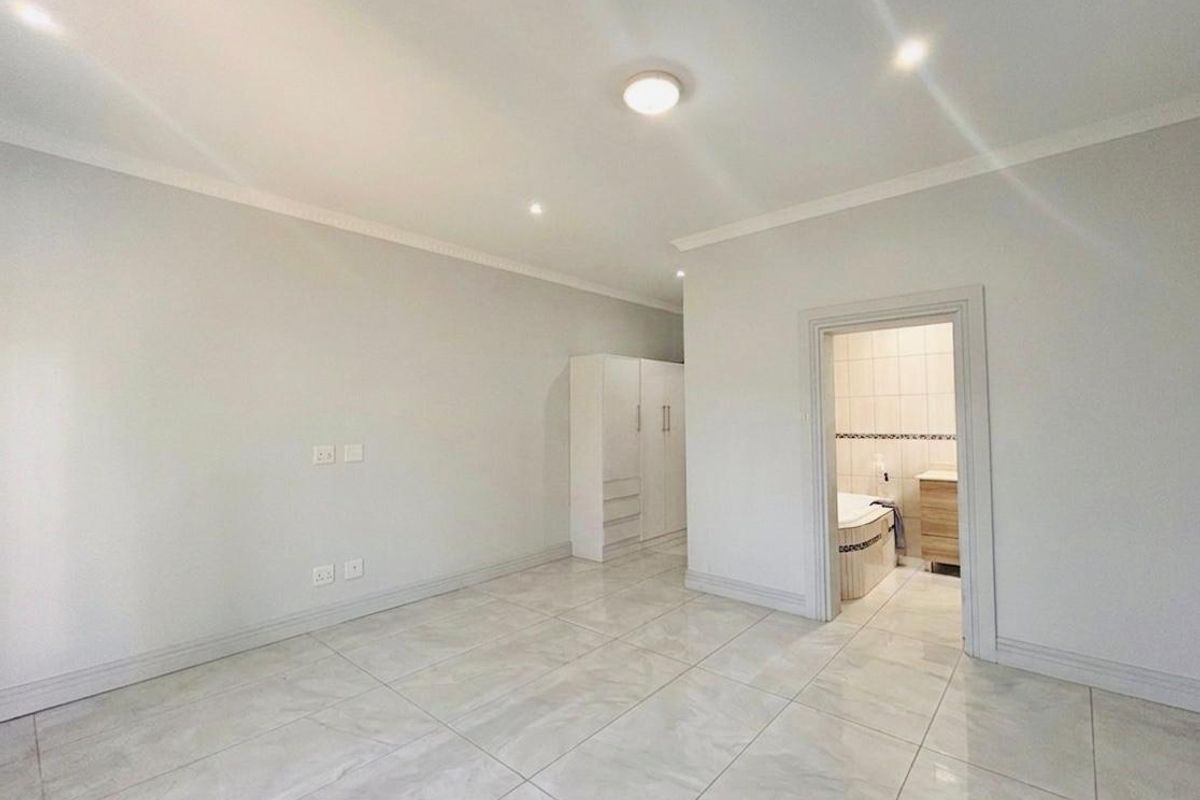 Spacious bedroom featuring large format floor tiles, built-in cabinetry, and direct access to an en-suite bathroom.