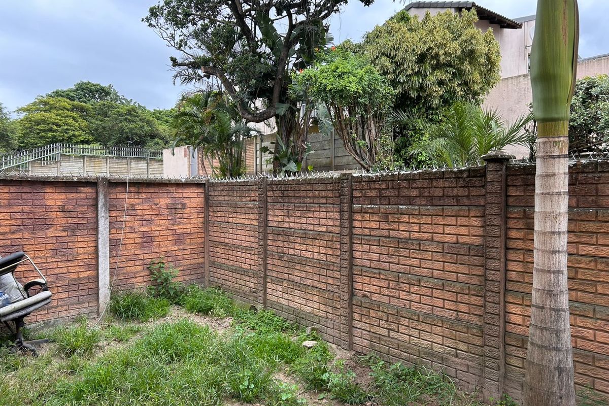 A private rear garden area featuring a high perimeter brick boundary wall with security spikes and established trees.
