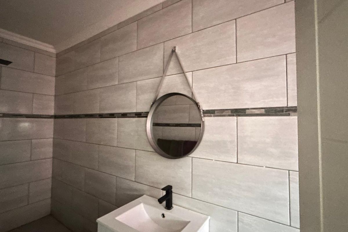 Modern bathroom featuring neutral wall tiling with a decorative accent strip, a contemporary vanity basin with a black faucet, and a circular wall mirror.
