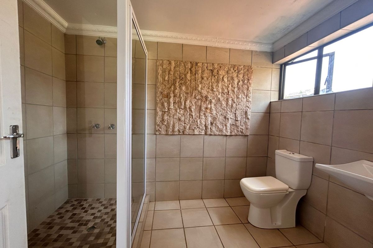 A functional bathroom featuring a glass-enclosed shower, a wall-mounted toilet, and a decorative stone feature wall with neutral floor-to-ceiling tiling.