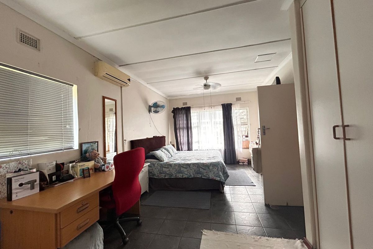 Spacious bedroom featuring tiled flooring, built-in cupboards, a ceiling fan, and a wall-mounted air conditioning unit.