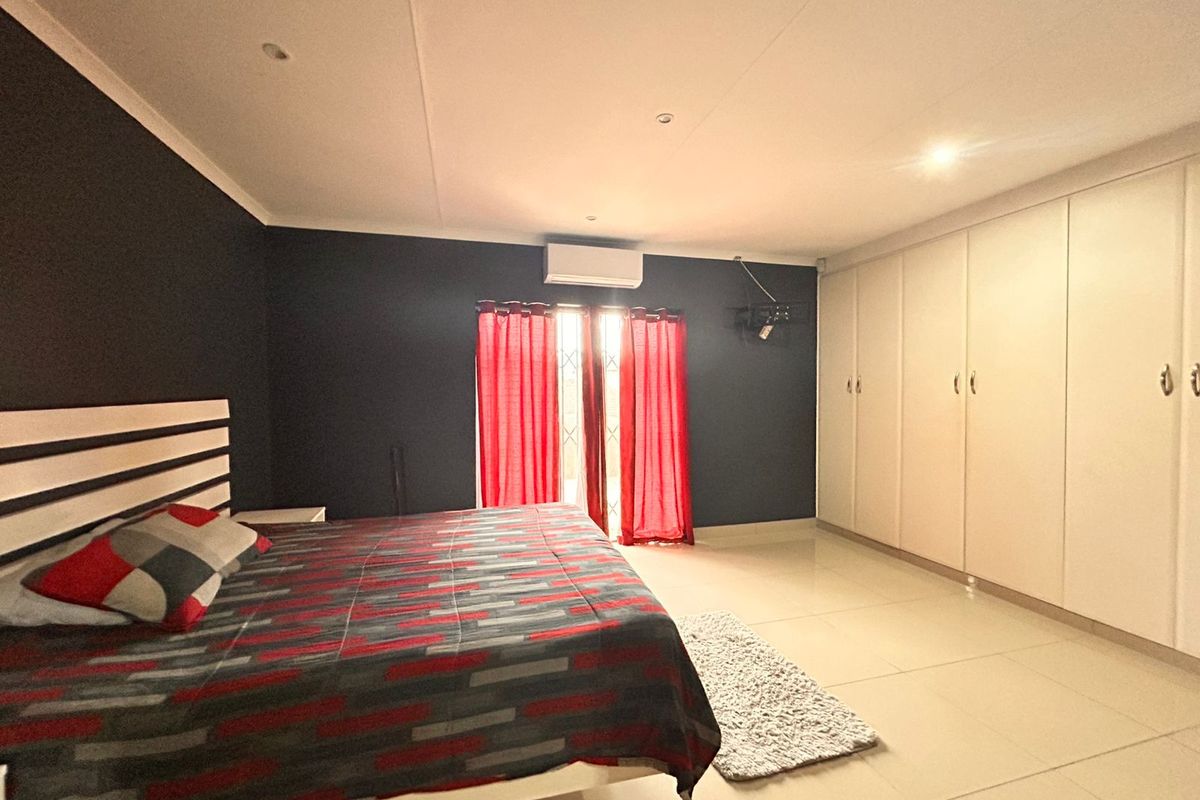 Spacious bedroom featuring large built-in cupboards, tiled flooring, recessed ceiling lighting, and a wall-mounted air conditioning unit.