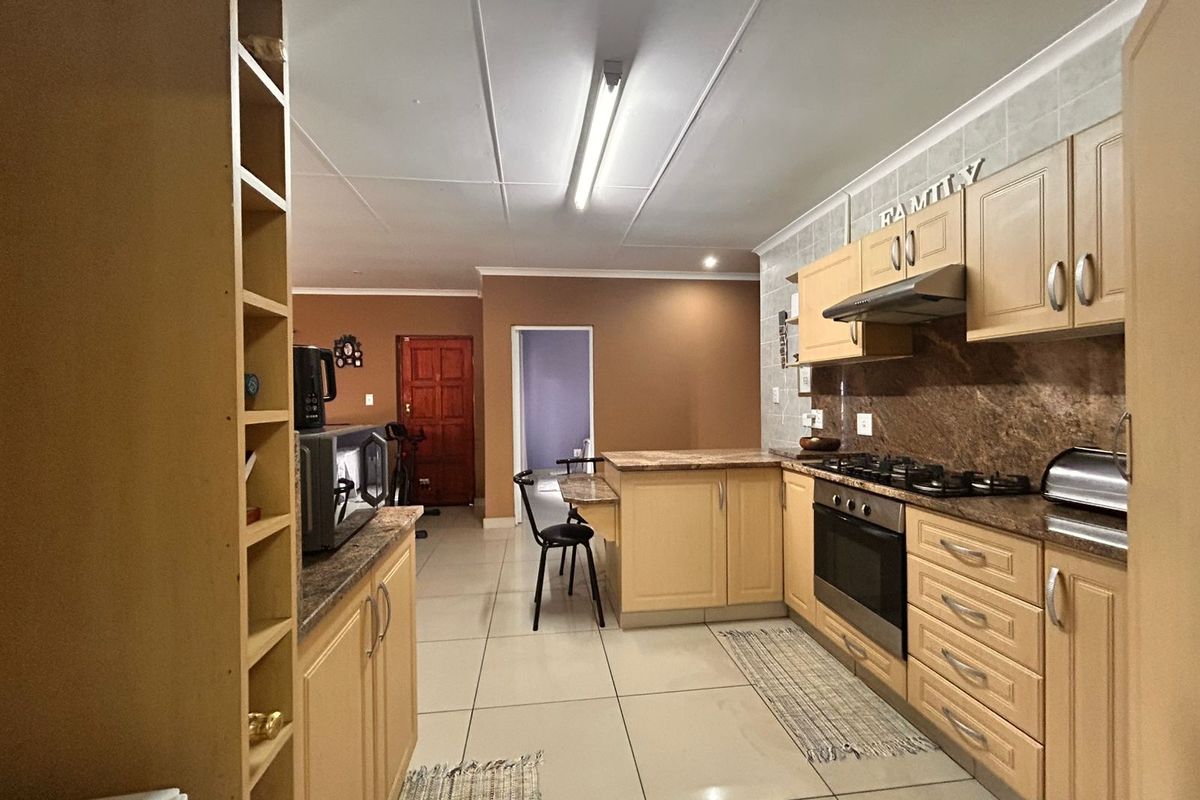 A functional kitchen featuring light wood cabinetry, granite countertops, a built-in oven, gas hob, and an extractor fan, with tiled flooring throughout.