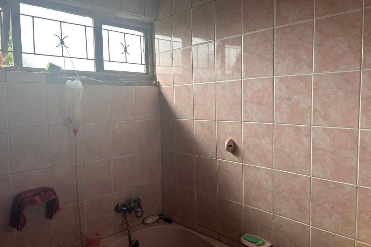 A dated bathroom featuring pink wall tiles, a matching bathtub, and a window with security bars.