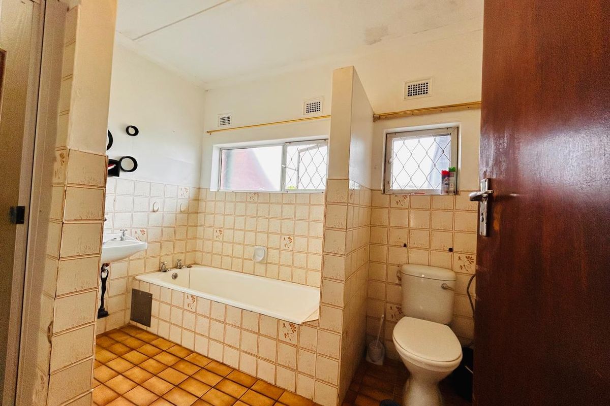 A dated bathroom featuring a built-in bathtub, pedestal basin, and toilet with original ceramic wall and floor tiling.