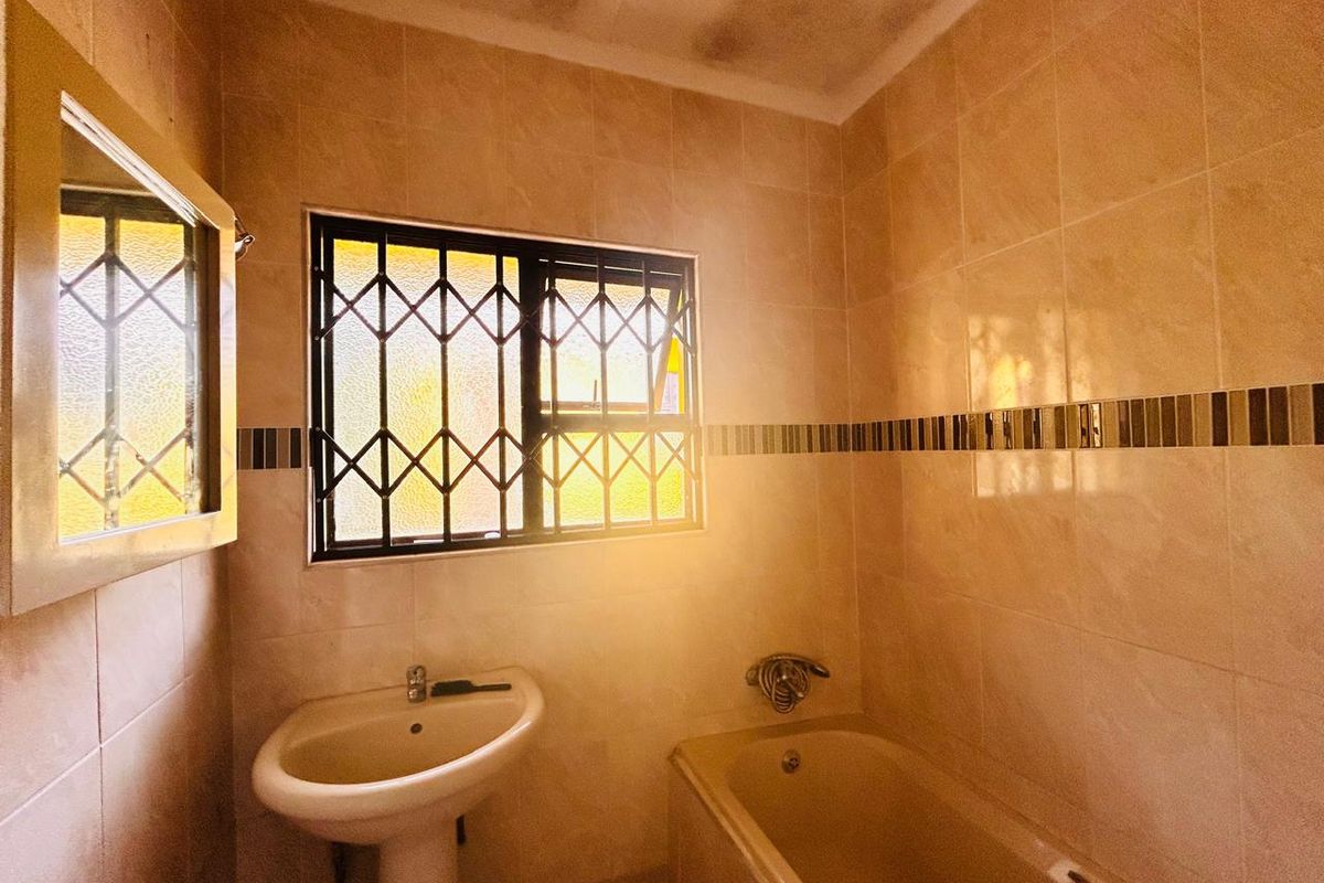 A dated bathroom featuring a pedestal basin, bathtub, and tiled walls with security bars on the window.