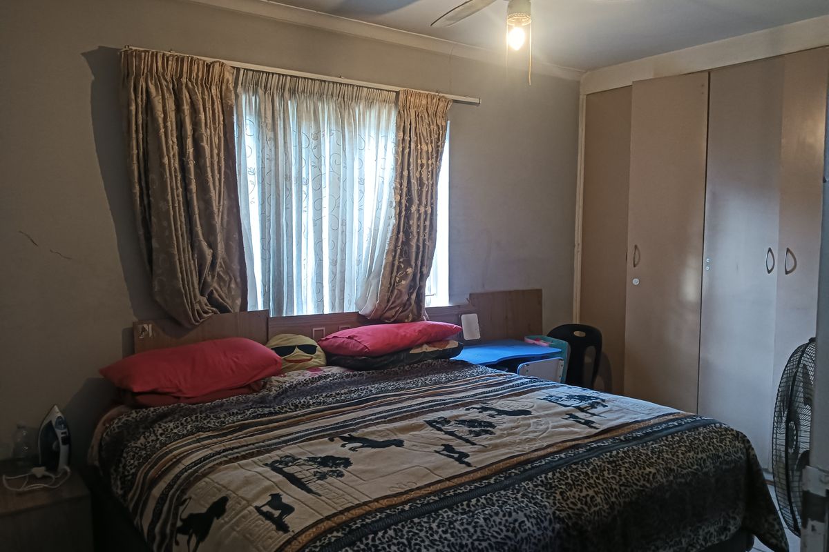 A bedroom featuring built-in cupboards, a ceiling fan, and a window with curtaining.