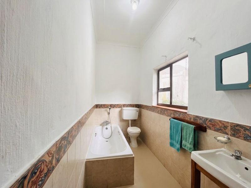 A functional bathroom featuring a bathtub, toilet, and washbasin with decorative tiled accents and natural light from a side window.