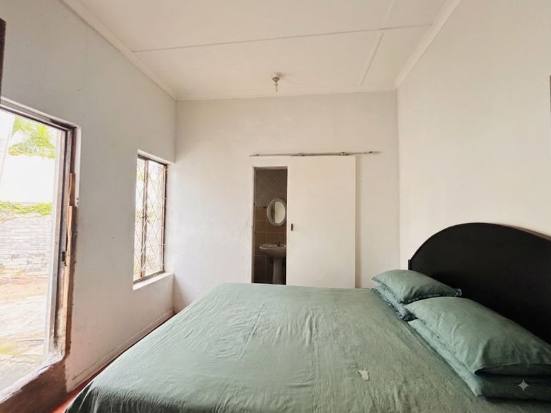 A bedroom featuring a sliding door with security gate and an en-suite bathroom with a pedestal basin.