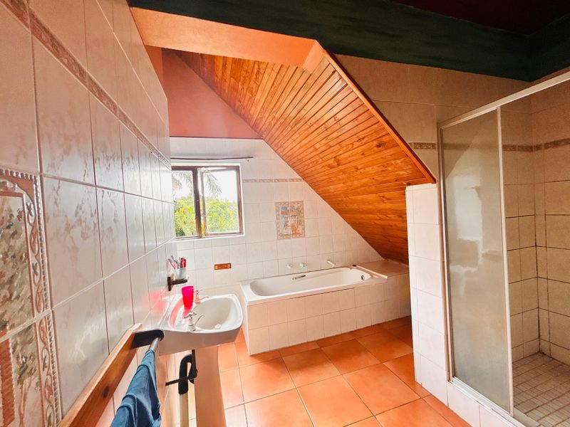 Bathroom featuring a pedestal basin, built-in bathtub, and separate shower enclosure under a vaulted timber-clad ceiling with tiled finishes.