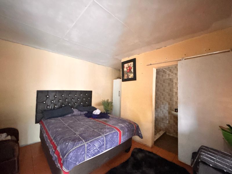 A bedroom featuring tiled flooring and an en-suite bathroom access point, requiring cosmetic updates to the walls and ceiling finishes.