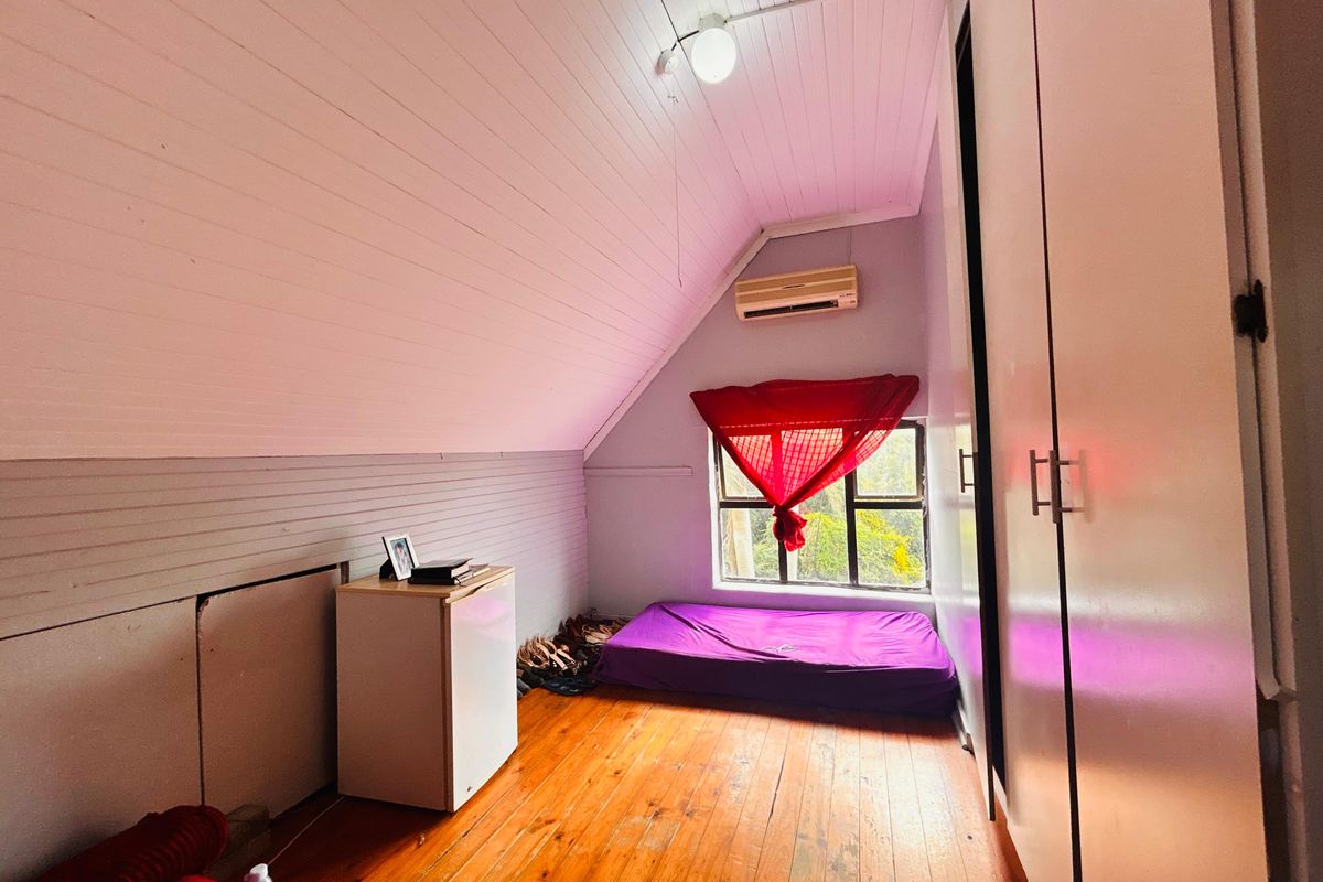 A bedroom featuring timber flooring, a sloped ceiling, built-in cupboards, and a wall-mounted air conditioning unit.