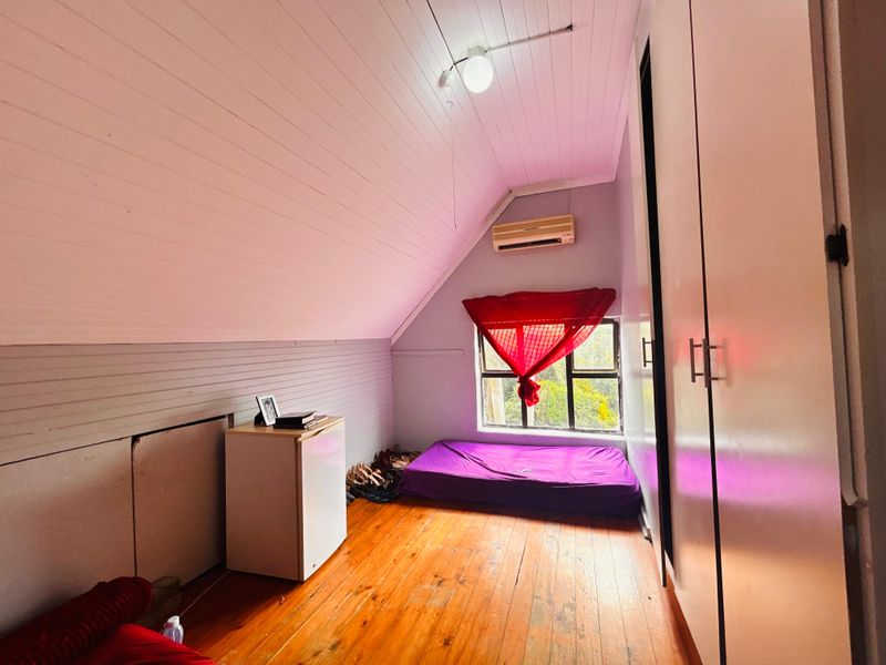 A bedroom featuring timber flooring, a sloped ceiling, built-in cupboards, and a wall-mounted air conditioning unit.