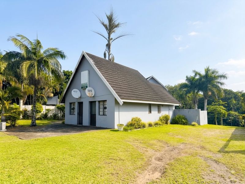 A detached house featuring a pitched tiled roof, grey exterior walls, and a surrounding lawn with a concrete driveway.