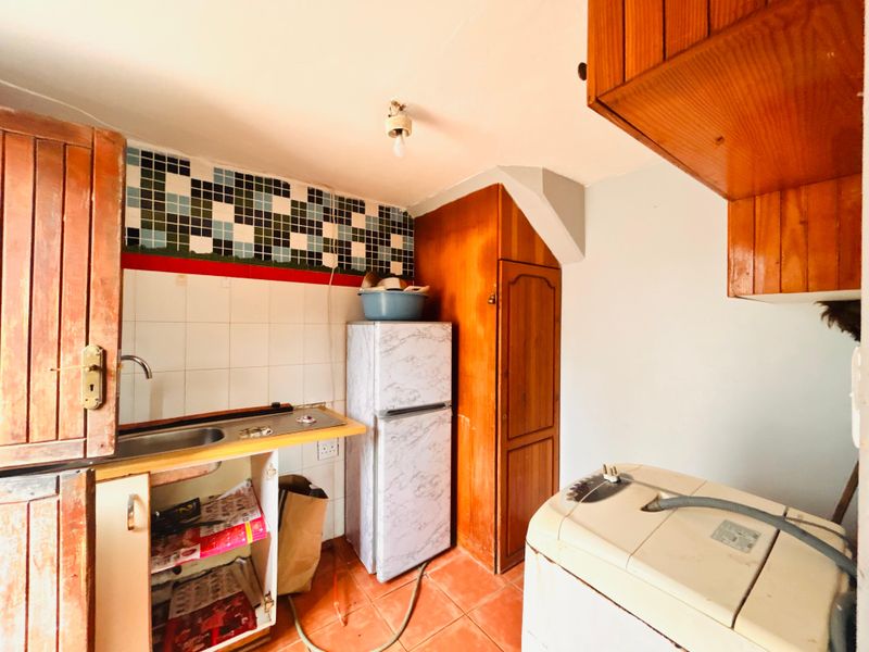 A functional laundry area featuring built-in wooden cabinetry, a stainless steel sink, and tiled splashback, requiring cosmetic updates to improve its condition.