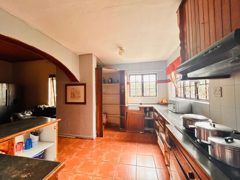A functional kitchen featuring tiled floors, built-in cabinetry, and an integrated hob with extractor fan, opening into an adjacent living area via an archway.