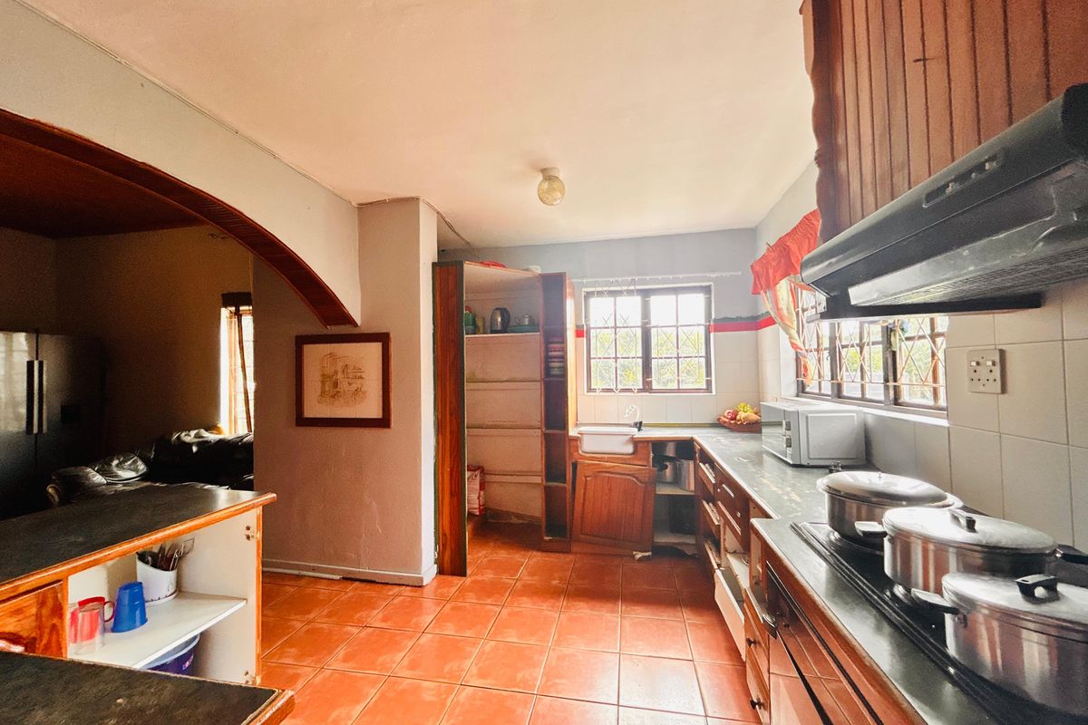 A functional kitchen featuring tiled floors, built-in cabinetry, and an integrated hob with extractor fan, opening into an adjacent living area via an archway.