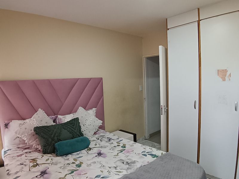 A bedroom featuring built-in cupboards, tiled flooring, and a ceiling light fixture, offering a functional space with potential for cosmetic updates.