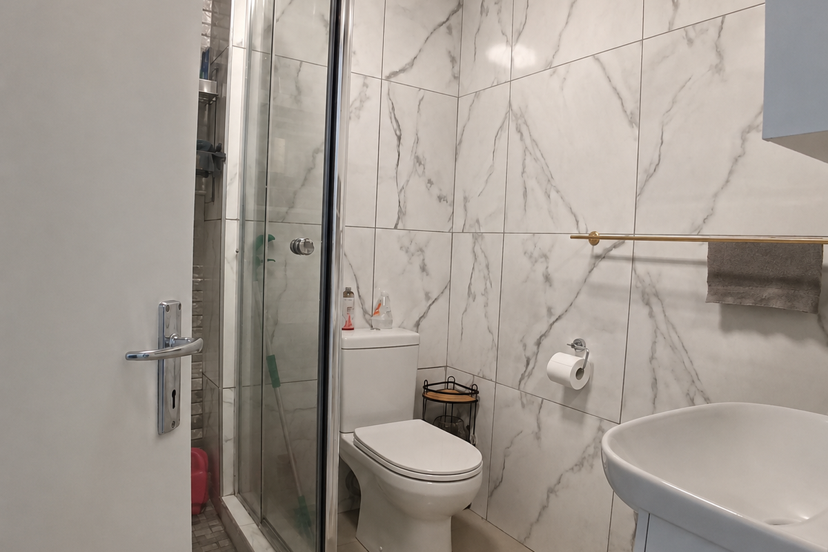 Modern bathroom featuring marble-effect wall tiles, a glass shower enclosure, a pedestal washbasin, and a toilet.