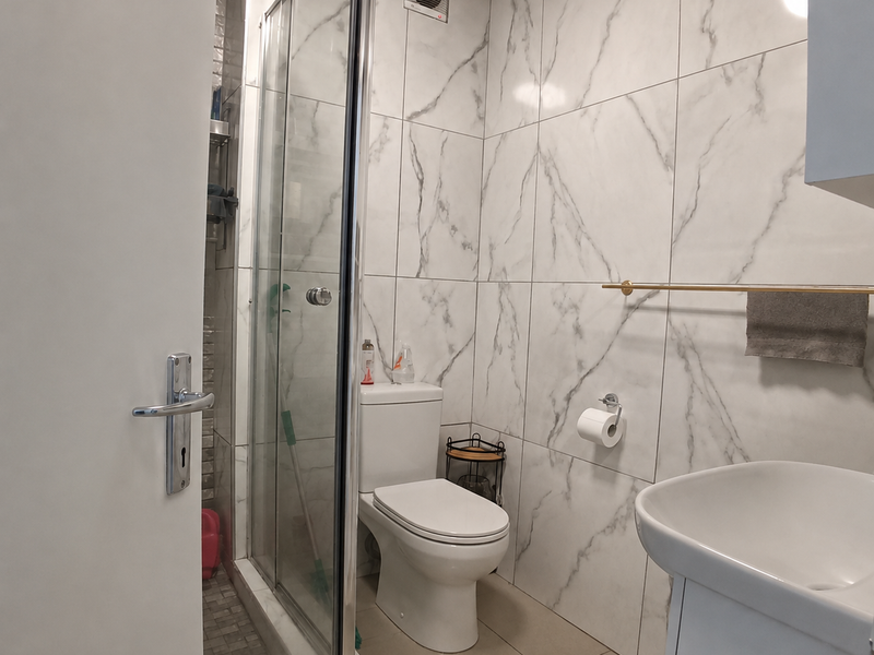 Modern bathroom featuring marble-effect wall tiles, a glass shower enclosure, a pedestal washbasin, and a toilet.