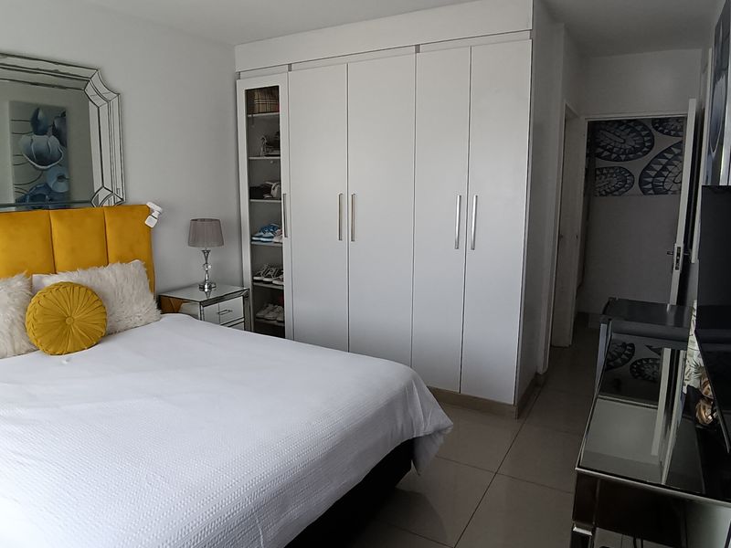 A well-maintained bedroom featuring neutral tiled flooring and a large, white built-in wardrobe providing ample storage space.