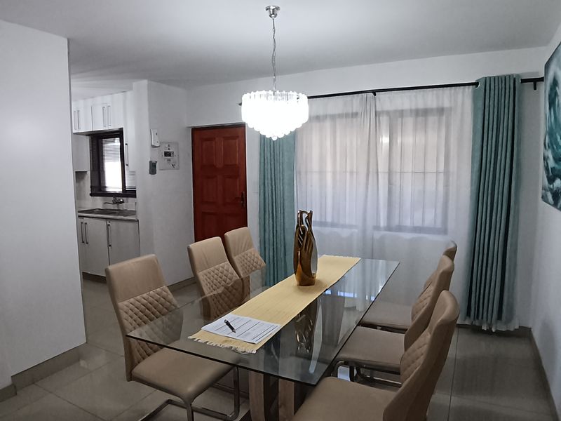 An open-plan dining area featuring tiled floors and a pendant light, with a view into the adjacent kitchen space.