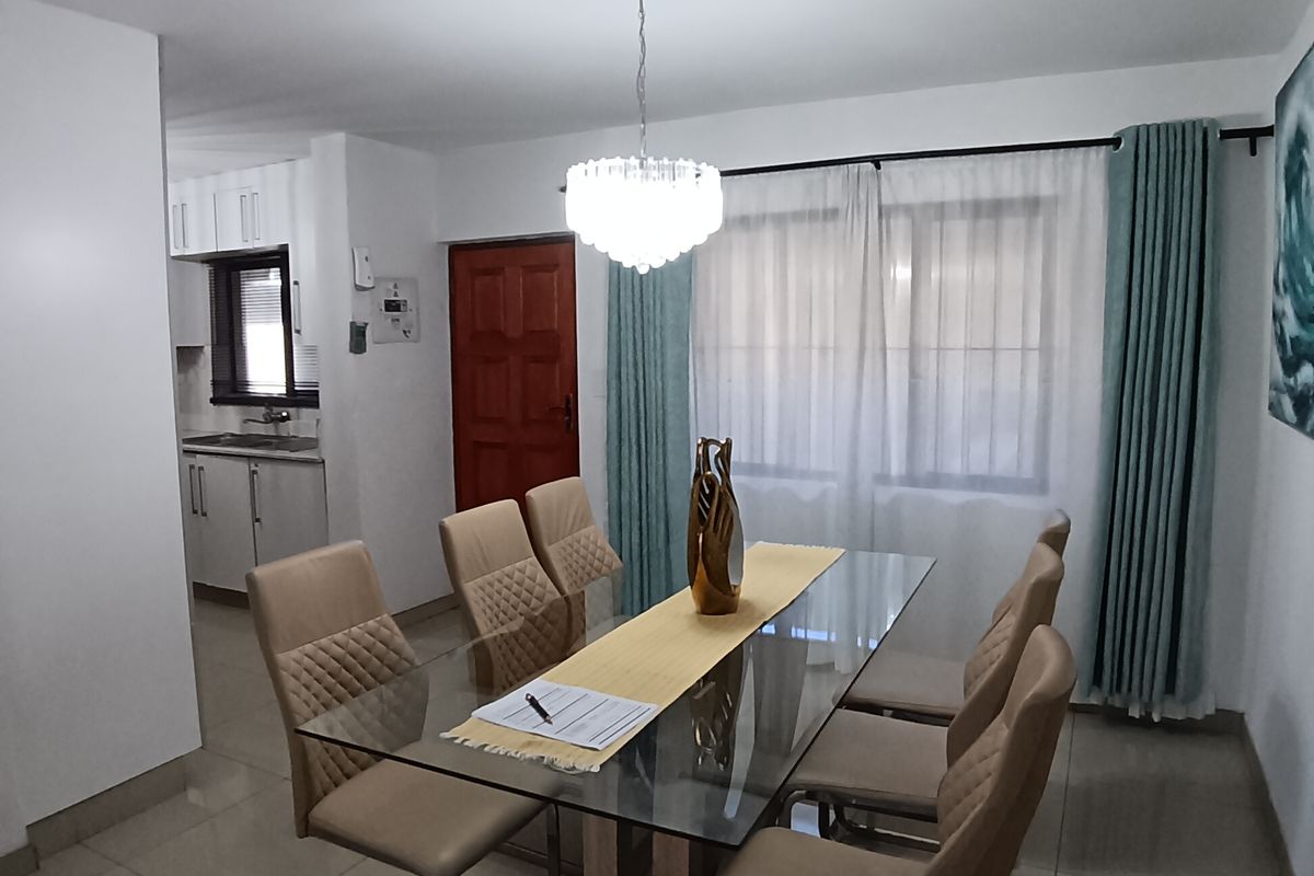 An open-plan dining area featuring tiled floors and a pendant light, with a view into the adjacent kitchen space.