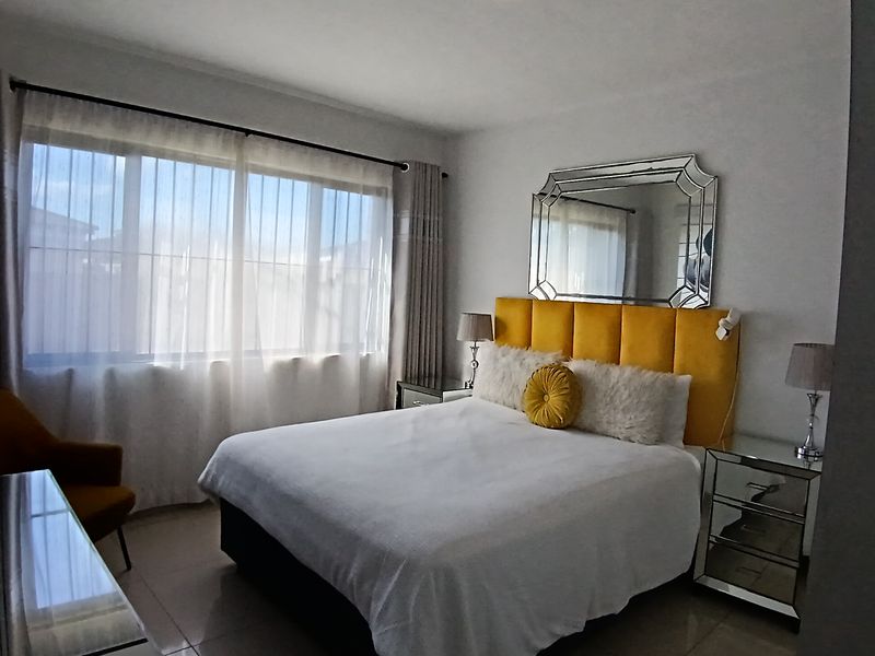 A well-lit bedroom featuring large windows, neutral tiled flooring, and a clean, modern aesthetic.