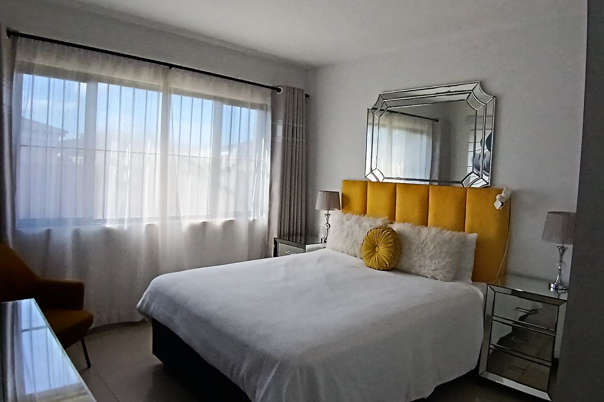 A well-lit bedroom featuring large windows, neutral tiled flooring, and a clean, modern aesthetic.