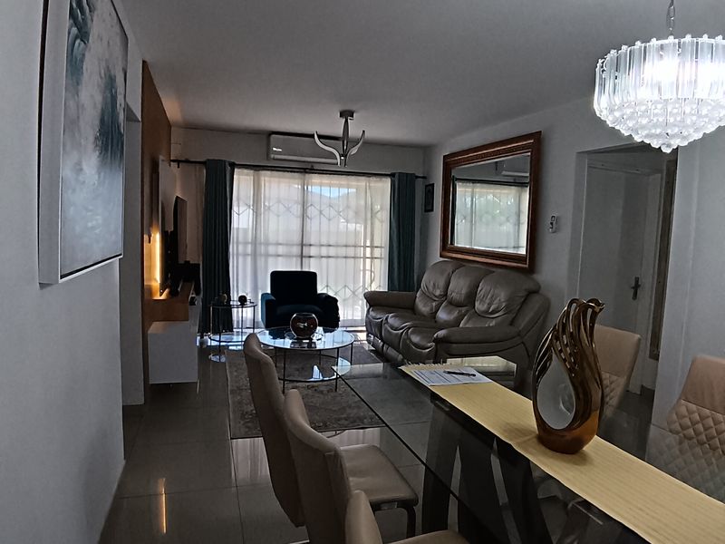 An open-plan living and dining area featuring polished tiled floors, a modern crystal chandelier, and a sliding glass door leading to a balcony.