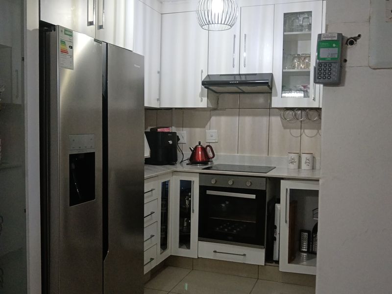 A compact, modern kitchen featuring white cabinetry, built-in oven and hob, extractor fan, and tiled flooring.