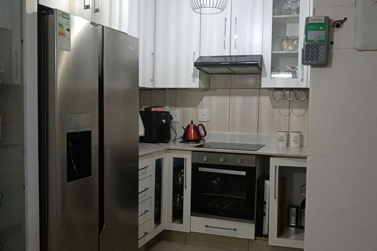 A compact, modern kitchen featuring white cabinetry, built-in oven and hob, extractor fan, and tiled flooring.