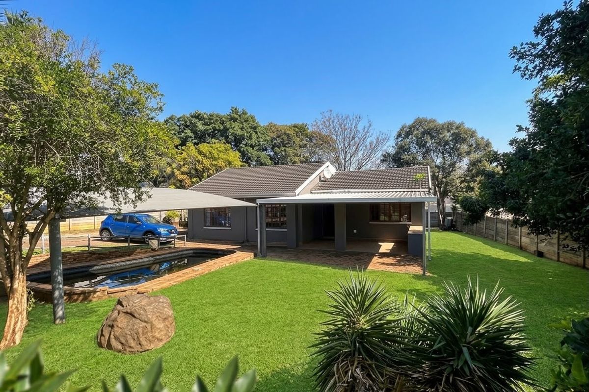 Rear view of the property featuring a well-maintained garden, swimming pool, covered patio area, and paved driveway space under a shade sail.