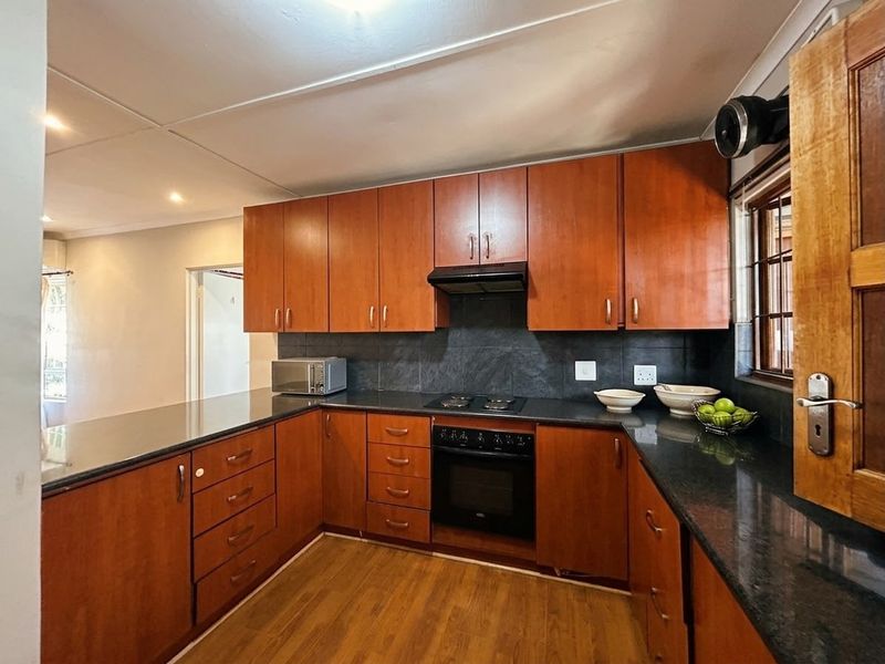 A functional kitchen featuring warm-toned wooden cabinetry, dark granite countertops, a built-in oven with hob, and a tiled backsplash.