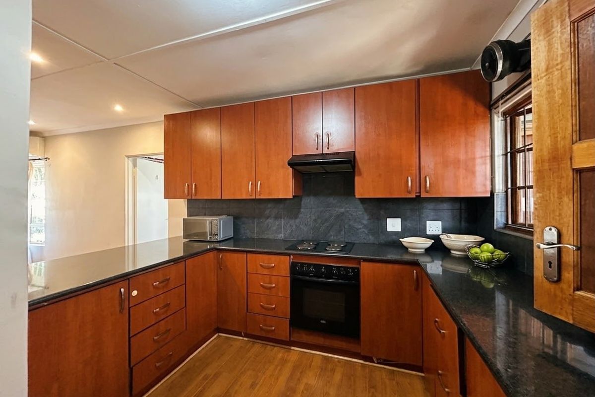 A functional kitchen featuring warm-toned wooden cabinetry, dark granite countertops, a built-in oven with hob, and a tiled backsplash.