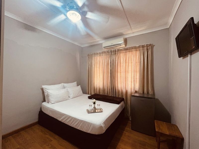 A compact bedroom featuring laminate flooring, a ceiling fan, and a wall-mounted air conditioning unit.