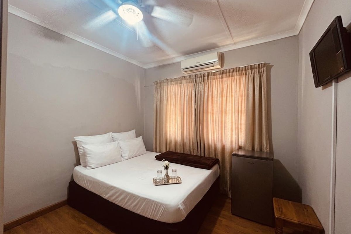 A compact bedroom featuring laminate flooring, a ceiling fan, and a wall-mounted air conditioning unit.