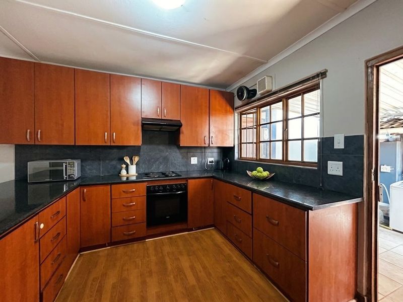 A functional kitchen featuring warm-toned wooden cabinetry, dark stone countertops, a built-in oven, gas hob, and a tiled backsplash.