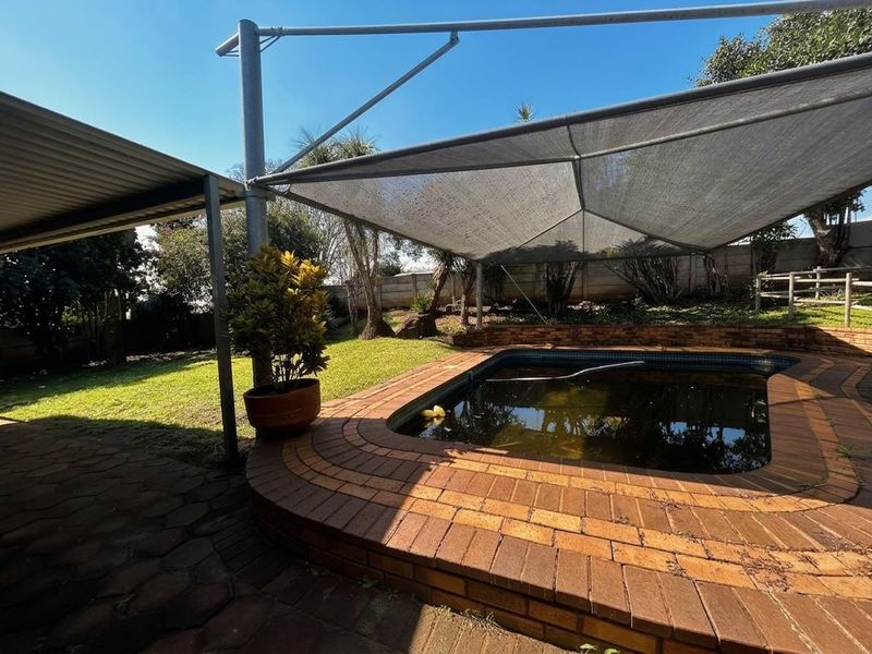 Outdoor pool area featuring a brick-edged swimming pool with a shade sail structure and adjacent paved patio space.