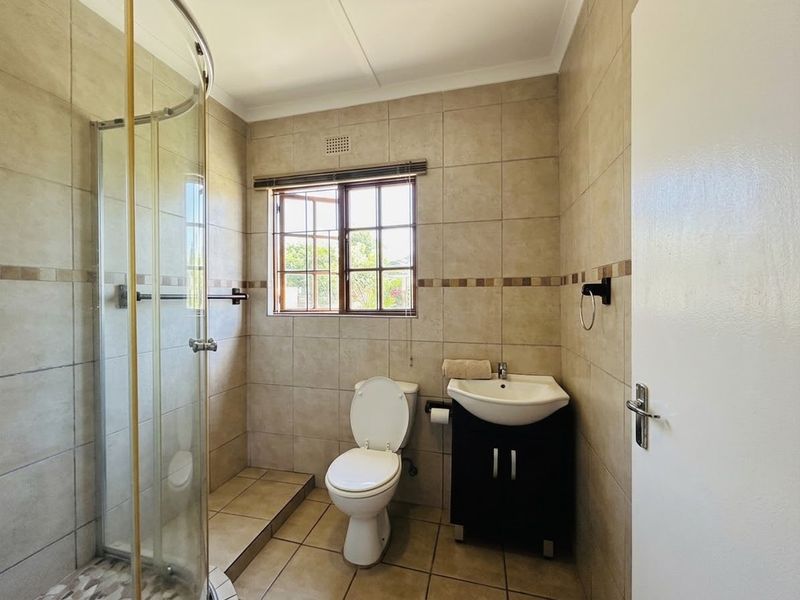 A functional bathroom featuring a glass shower enclosure, a vanity basin, and neutral wall and floor tiling with a window for natural light.