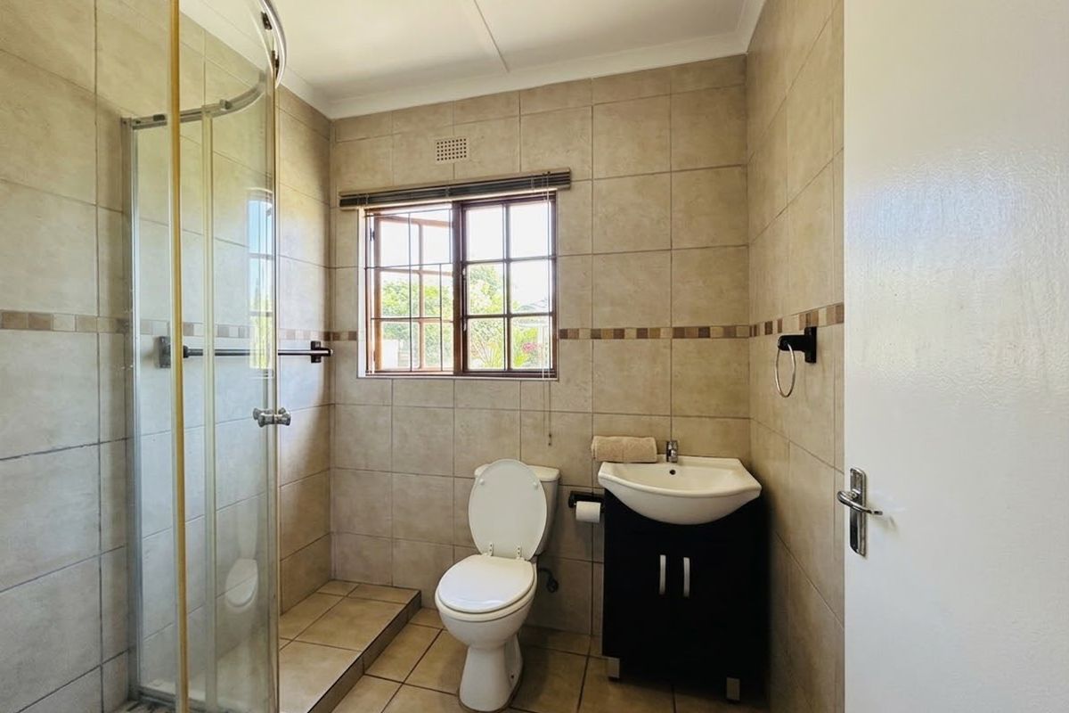 A functional bathroom featuring a glass shower enclosure, a vanity basin, and neutral wall and floor tiling with a window for natural light.