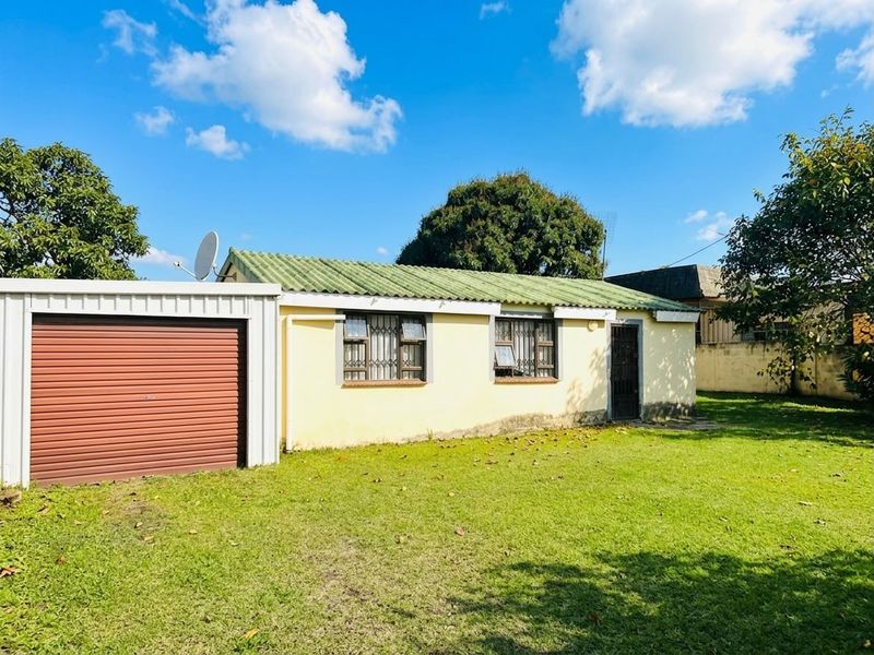 Rear view of the property featuring a detached metal garage, tiled roof, and a spacious garden area with boundary walling.