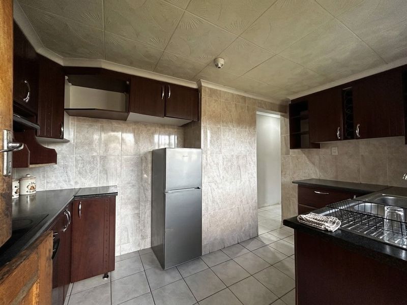 A functional kitchen featuring dark wood cabinetry, tiled walls, and tiled flooring, currently showing signs of wear and missing cabinet components.
